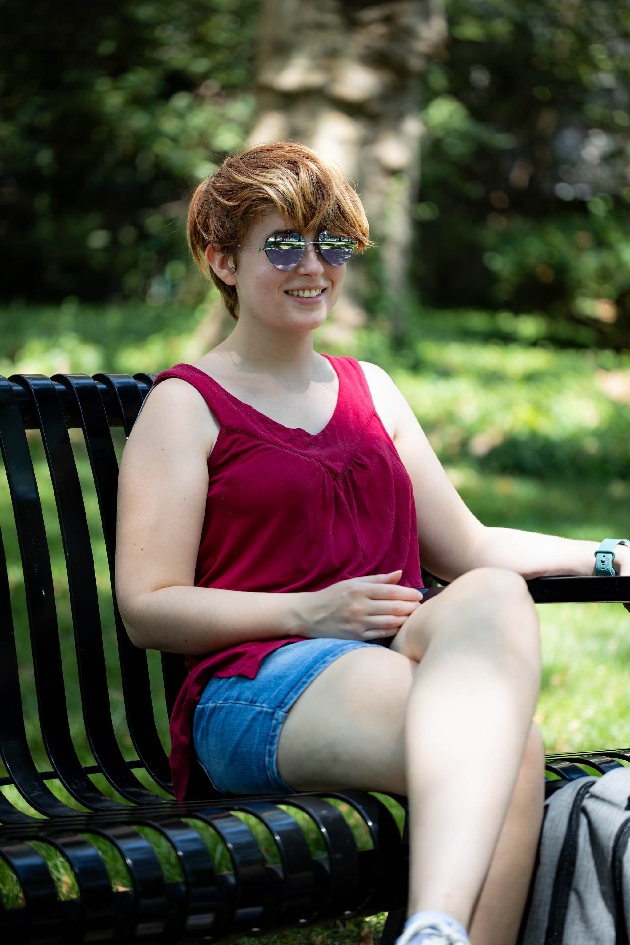 Person sitting on bench with heart sunglasses, red tank top, and short jean shorts.